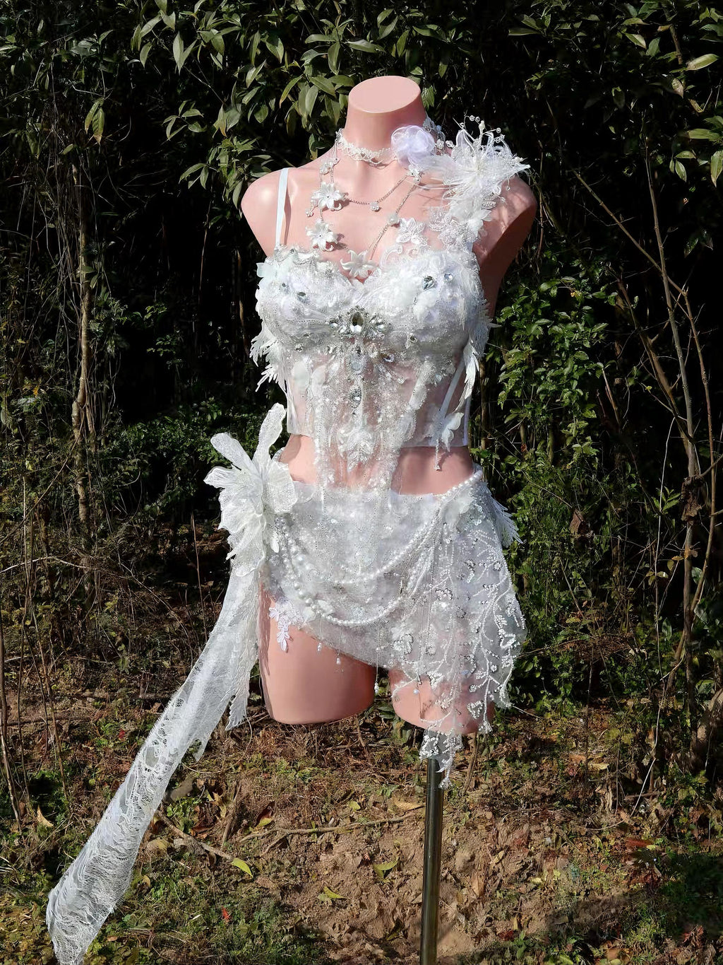 Elegant white lace lingerie set with floral appliqués and sheer detailing, displayed on mannequin outdoors